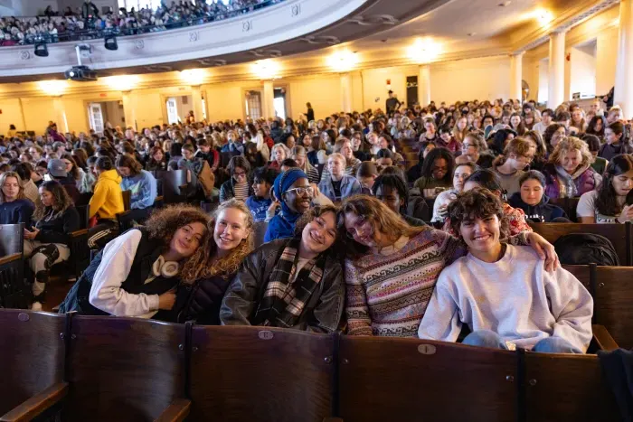 A group of five students smile for the camera, surrounded by many other students in attendance at Cromwell Day, all seated in the auditorium.