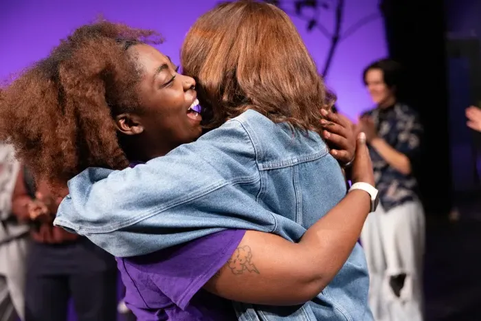 A side-view of two students embraced in a hug, one student smiles enthusiastically.