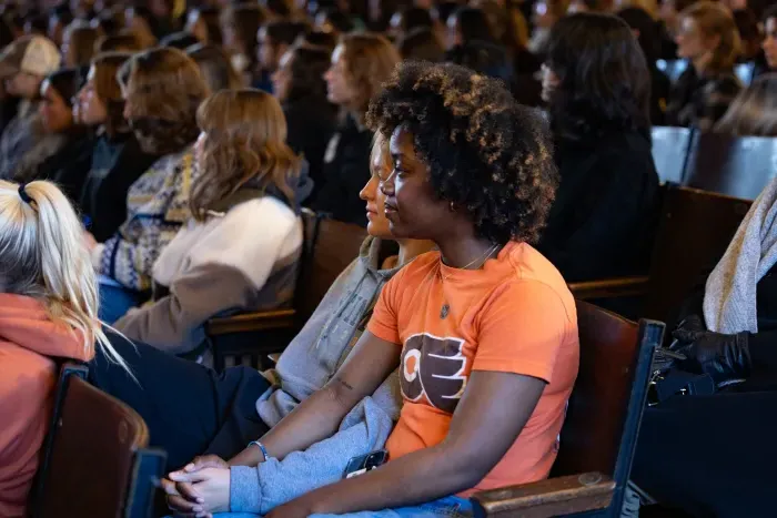 Two students sit in an auditorium holding hands.